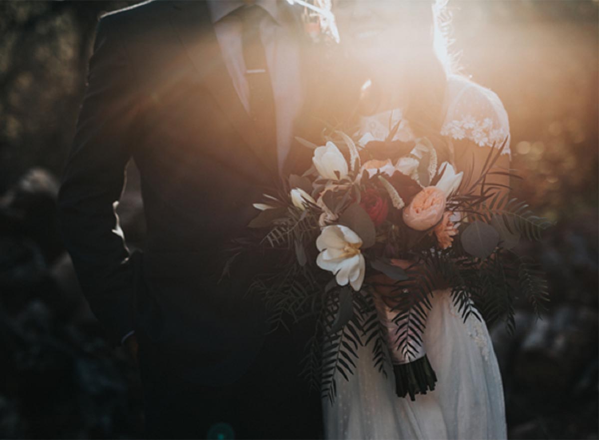 Wedded couple with bride holding flowers and sunshine ray falling on them
